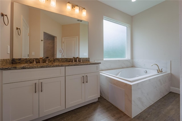 bathroom with tiled bath, wood-type flooring, and vanity