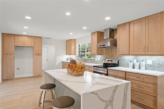 kitchen featuring wall chimney exhaust hood, stainless steel stove, light stone countertops, a center island, and light wood-type flooring