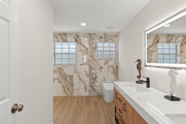 bathroom with tile walls, vanity, wood-type flooring, and toilet