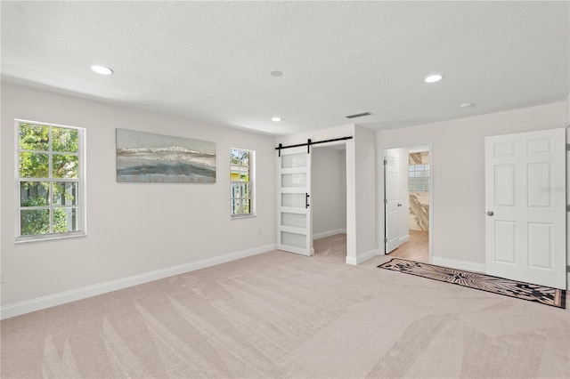 unfurnished bedroom with connected bathroom, a textured ceiling, a barn door, and light colored carpet