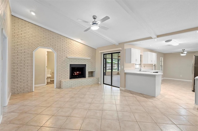 unfurnished living room with light tile patterned floors, a fireplace, brick wall, and vaulted ceiling with beams