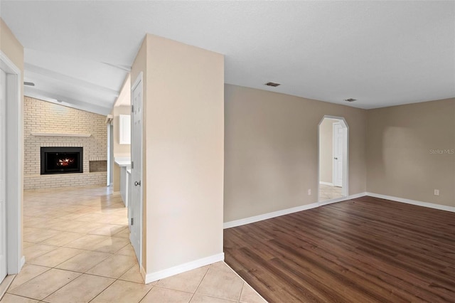 spare room with brick wall, light hardwood / wood-style floors, and a fireplace