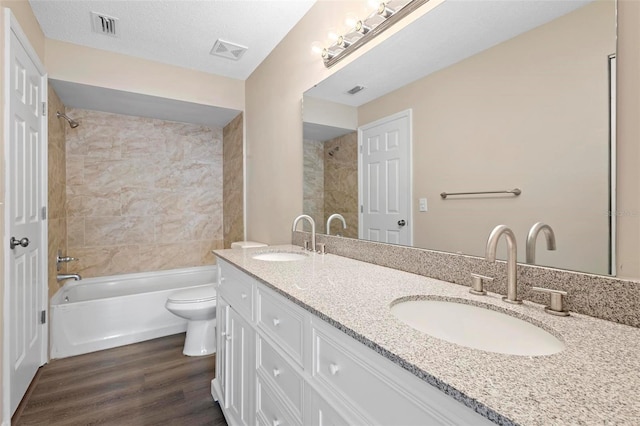 full bathroom featuring a textured ceiling, wood-type flooring, vanity, toilet, and tiled shower / bath combo