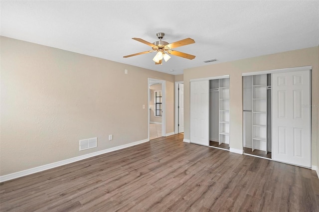 unfurnished bedroom featuring dark wood-type flooring, ceiling fan, and multiple closets