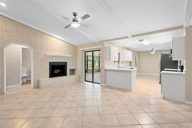 unfurnished living room with a fireplace, brick wall, light tile patterned flooring, and lofted ceiling with beams