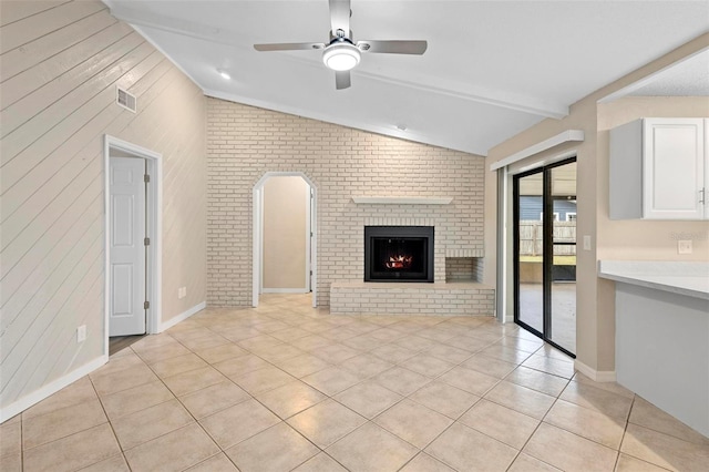 unfurnished living room featuring light tile patterned flooring, brick wall, ceiling fan, vaulted ceiling with beams, and a brick fireplace