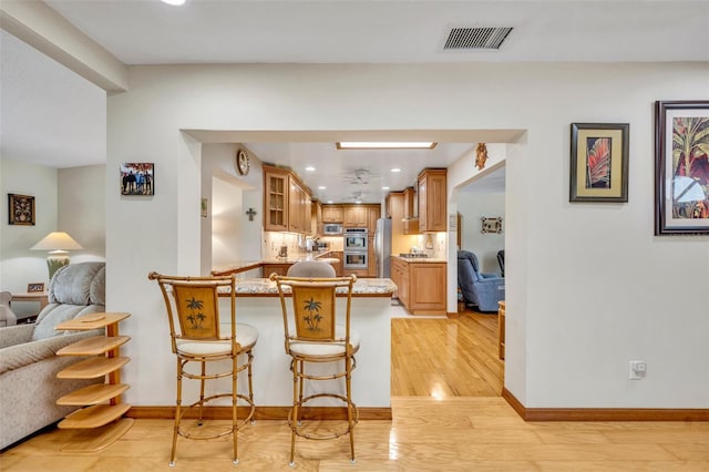 kitchen with kitchen peninsula, a kitchen breakfast bar, light hardwood / wood-style floors, and appliances with stainless steel finishes