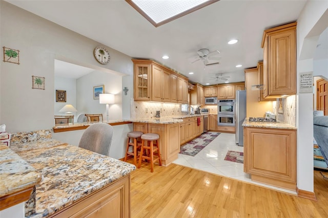 kitchen featuring a kitchen bar, kitchen peninsula, light stone counters, and light hardwood / wood-style flooring