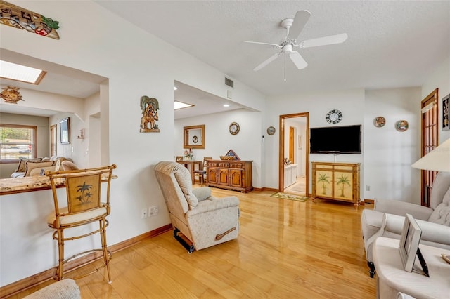 living room featuring ceiling fan, wood-type flooring, a textured ceiling, and a skylight