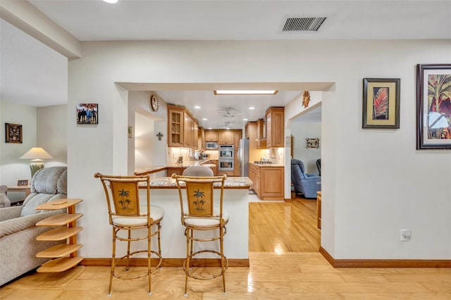 kitchen with stainless steel appliances, visible vents, light wood-style flooring, glass insert cabinets, and a peninsula