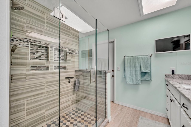 bathroom with a stall shower, wood finished floors, vanity, and baseboards