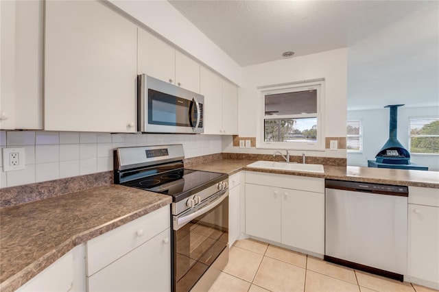 kitchen featuring light tile patterned flooring, sink, appliances with stainless steel finishes, a wood stove, and white cabinets