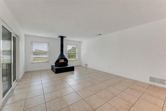 unfurnished living room featuring a wood stove and light tile patterned flooring