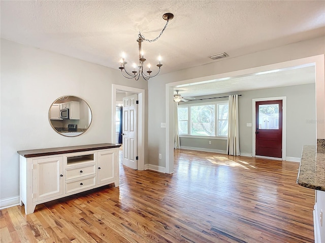 unfurnished dining area with light hardwood / wood-style flooring, a textured ceiling, and ceiling fan with notable chandelier