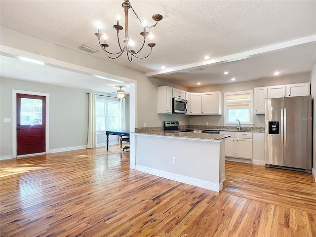 kitchen with white cabinets, light wood-type flooring, stone countertops, decorative light fixtures, and stainless steel appliances