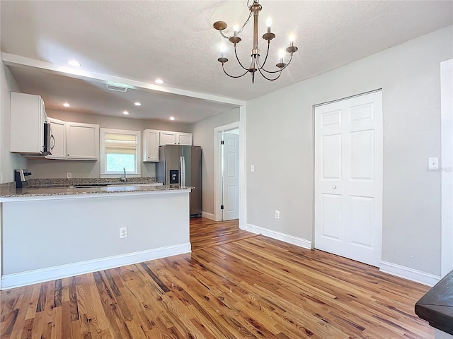 kitchen with a textured ceiling, white cabinets, stainless steel appliances, and light hardwood / wood-style floors