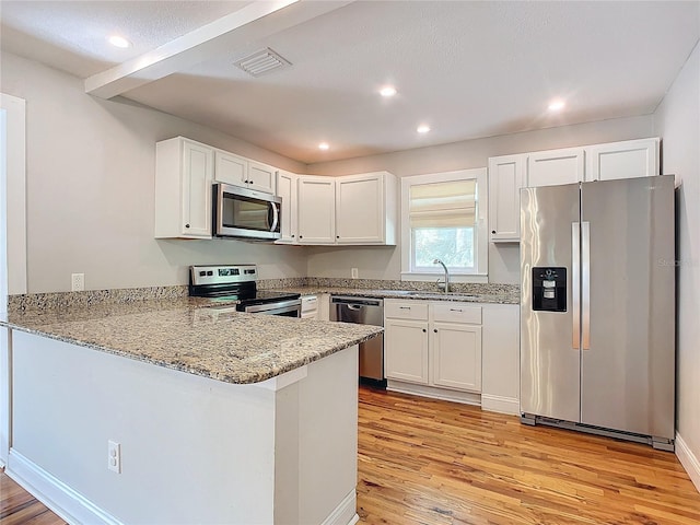 kitchen with light hardwood / wood-style flooring, kitchen peninsula, stainless steel appliances, and white cabinets