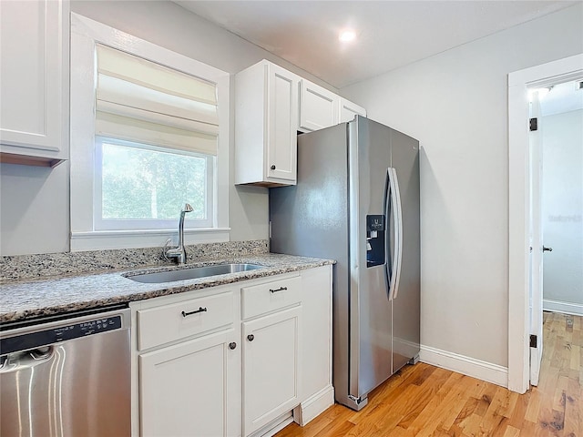 kitchen with white cabinets, appliances with stainless steel finishes, light stone countertops, light wood-type flooring, and sink