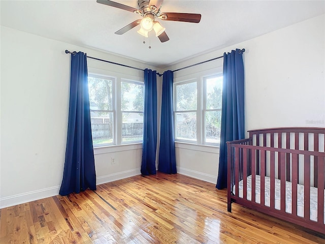 bedroom with light hardwood / wood-style flooring, multiple windows, a crib, and ceiling fan