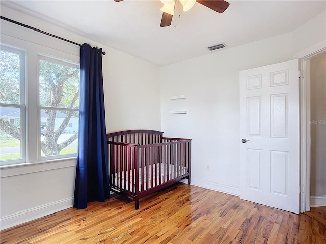 bedroom with a crib, light wood-type flooring, and ceiling fan