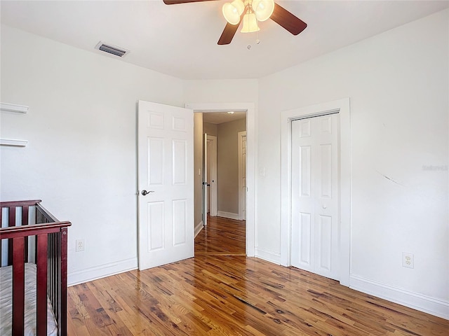 unfurnished bedroom featuring a closet, ceiling fan, wood-type flooring, and a nursery area