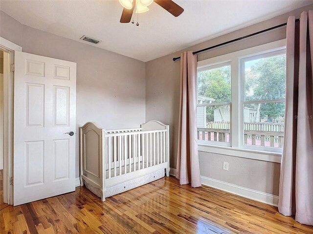 unfurnished bedroom with light hardwood / wood-style flooring, a nursery area, and ceiling fan