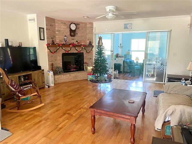 living room with a brick fireplace, ceiling fan, ornamental molding, a textured ceiling, and wood-type flooring