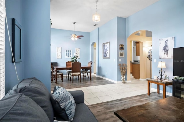 living room with a towering ceiling, light wood-type flooring, and ceiling fan