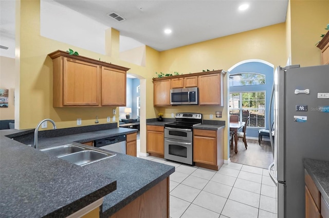 kitchen with appliances with stainless steel finishes, a towering ceiling, sink, and light tile patterned floors