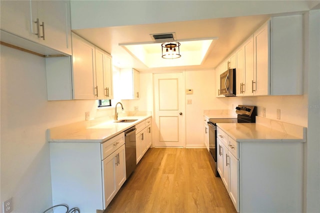 kitchen featuring stainless steel appliances, sink, a raised ceiling, white cabinetry, and light hardwood / wood-style floors