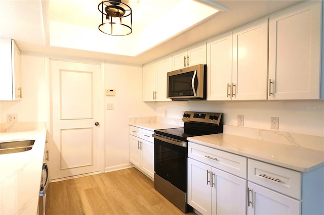 kitchen featuring white cabinetry, light stone countertops, a tray ceiling, light wood-type flooring, and stainless steel appliances