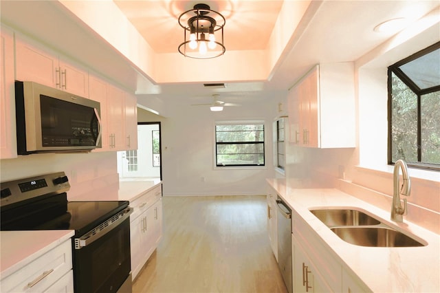 kitchen with white cabinets, a raised ceiling, appliances with stainless steel finishes, light wood-type flooring, and sink