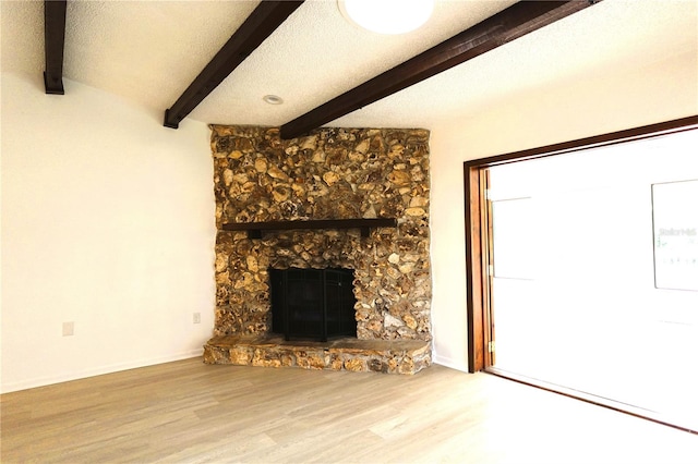 unfurnished living room featuring a textured ceiling, beamed ceiling, wood-type flooring, and a fireplace