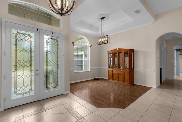 entrance foyer with ornamental molding, a tray ceiling, french doors, and light hardwood / wood-style floors