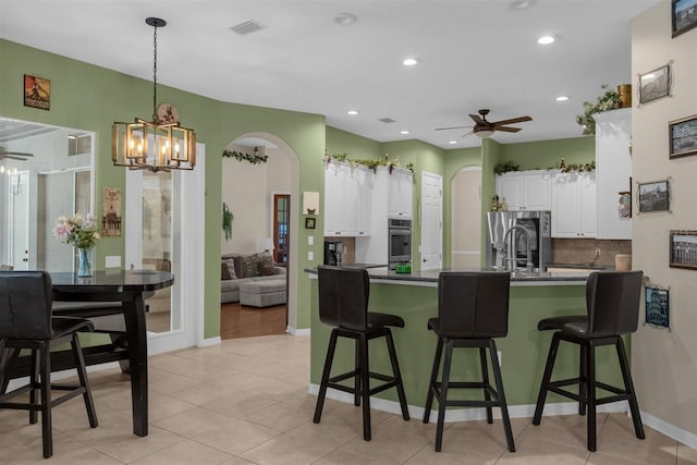 kitchen featuring ceiling fan with notable chandelier, stainless steel refrigerator with ice dispenser, kitchen peninsula, a breakfast bar, and white cabinetry