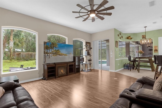 living room with light wood-type flooring, a wealth of natural light, a fireplace, and ceiling fan with notable chandelier