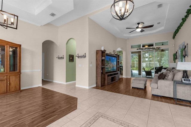 living room with a towering ceiling, ceiling fan with notable chandelier, light hardwood / wood-style flooring, and a tray ceiling