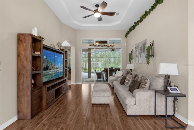 living room with dark hardwood / wood-style flooring, a tray ceiling, and ceiling fan