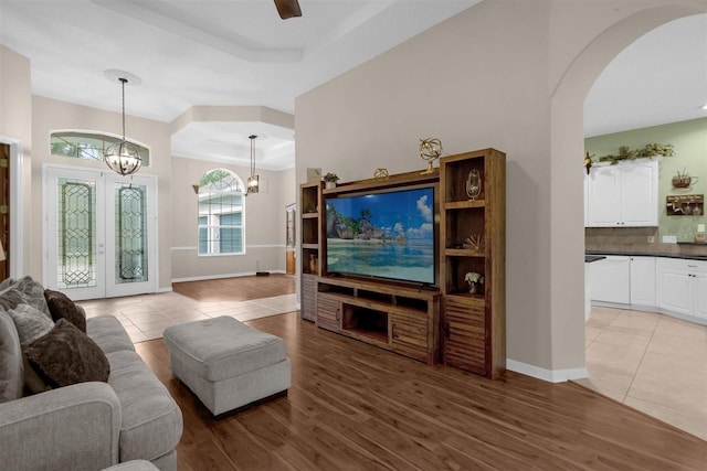 living room with ceiling fan with notable chandelier, a raised ceiling, light hardwood / wood-style flooring, and french doors