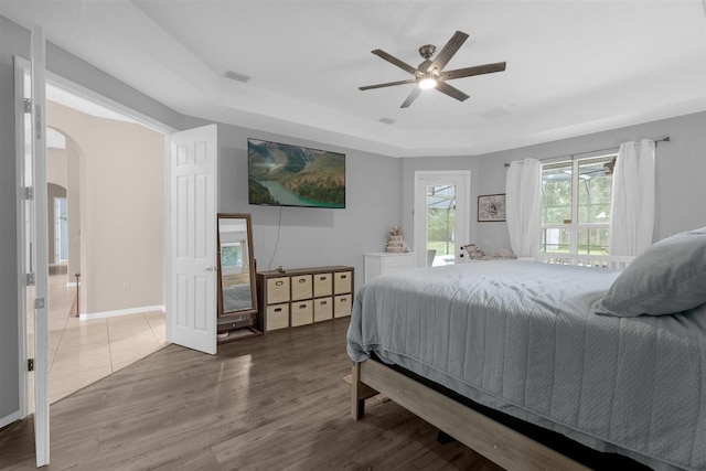 bedroom with hardwood / wood-style floors, ceiling fan, and a tray ceiling