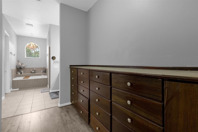 bathroom with a chandelier, tiled bath, and wood-type flooring