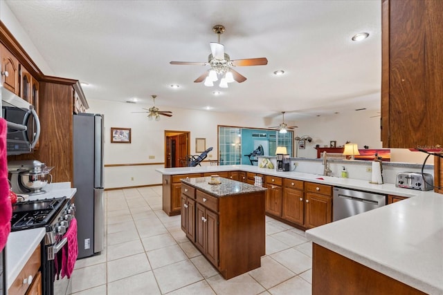 kitchen with light tile patterned floors, appliances with stainless steel finishes, kitchen peninsula, and a kitchen island