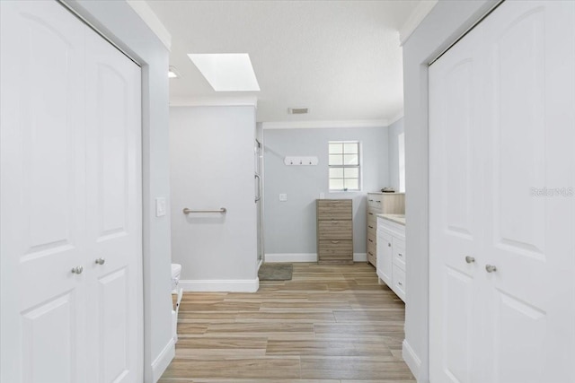 bathroom with vanity, a skylight, hardwood / wood-style floors, and ornamental molding