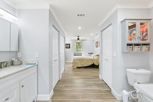 bathroom with wood-type flooring, crown molding, vanity, toilet, and ceiling fan