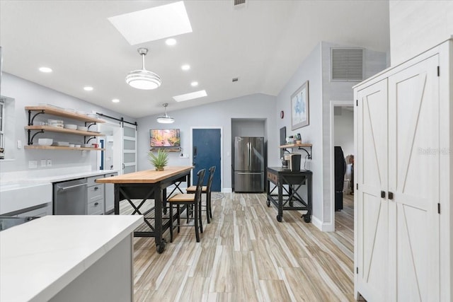 kitchen with light wood-type flooring, appliances with stainless steel finishes, a barn door, decorative light fixtures, and lofted ceiling with skylight