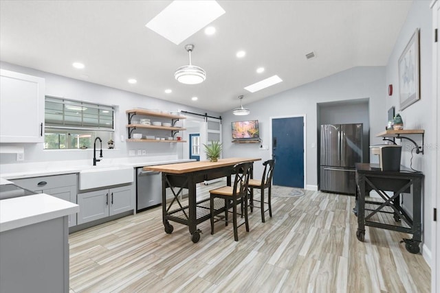 kitchen with gray cabinetry, stainless steel appliances, hanging light fixtures, sink, and lofted ceiling with skylight