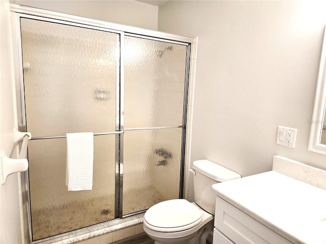 bathroom featuring toilet, vanity, and a shower with door