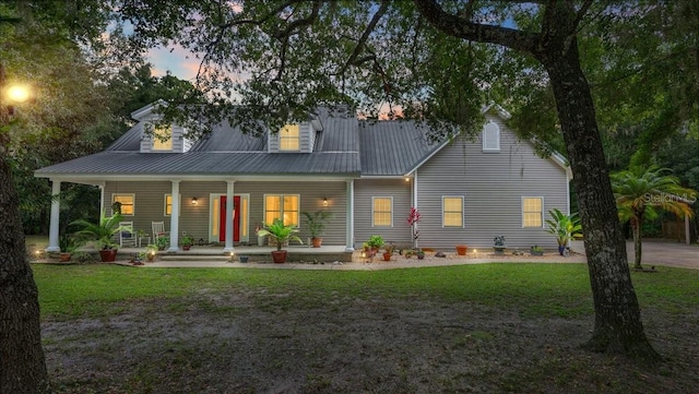 back house at dusk with a lawn and a porch