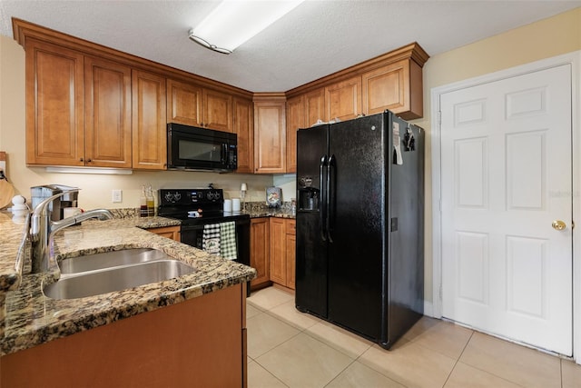 kitchen with sink, dark stone countertops, a textured ceiling, light tile patterned flooring, and black appliances