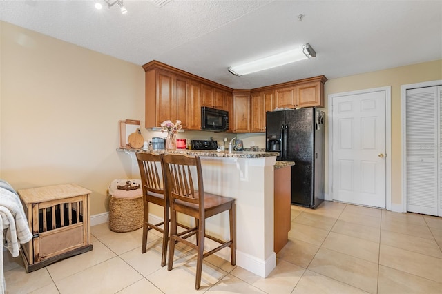 kitchen featuring light stone countertops, a kitchen breakfast bar, kitchen peninsula, a textured ceiling, and black appliances